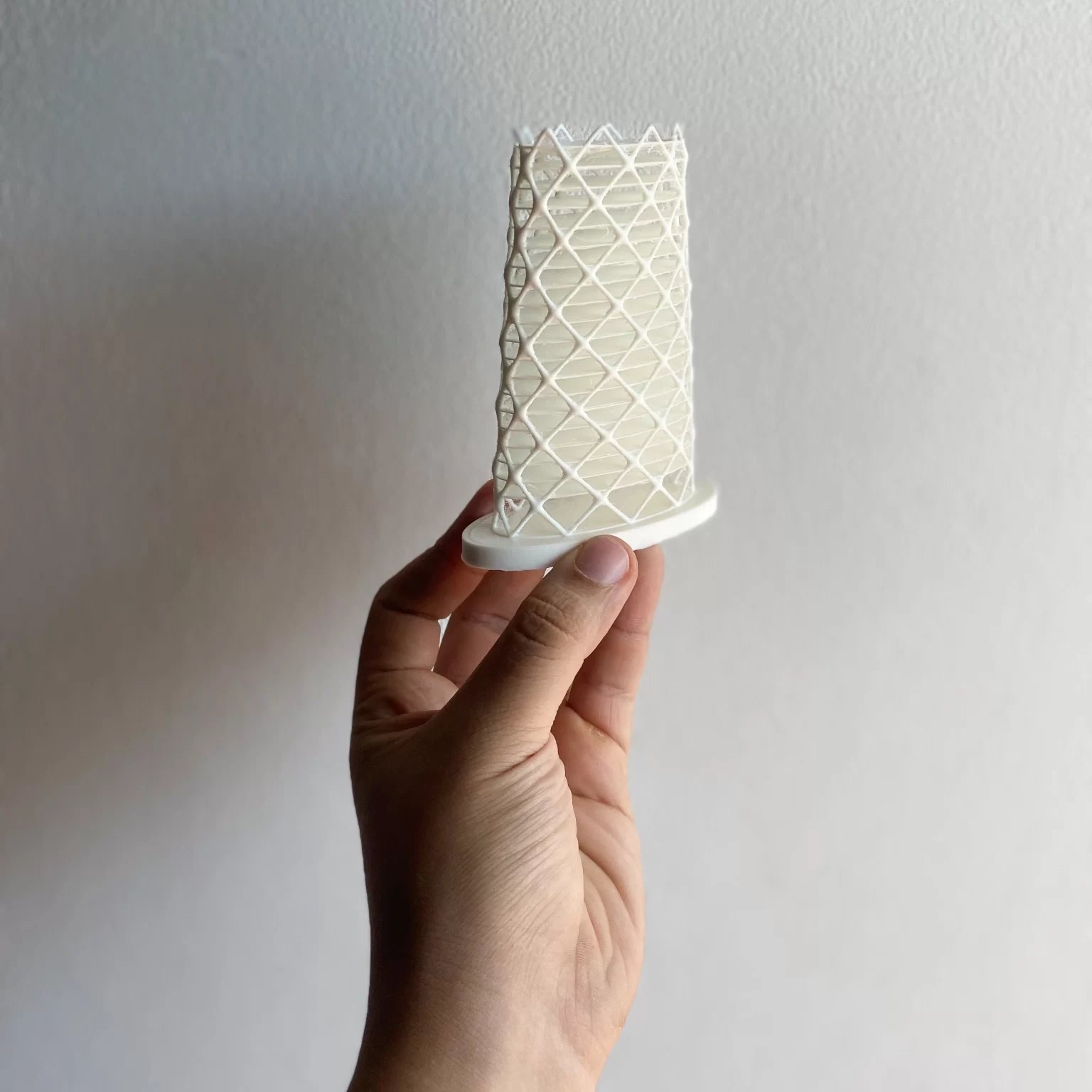 Modelo físico branco da Fachada Flow, com malha externa curva, segurado na mão.